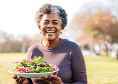 Woman smiling while holding plate of salad outside